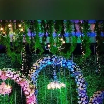 A closer look at the floral arches against the green wall, illuminated with soft blue and purple lighting. This combination of colorful flowers and dynamic lighting creates a vibrant and magical atmosphere for an evening reception.