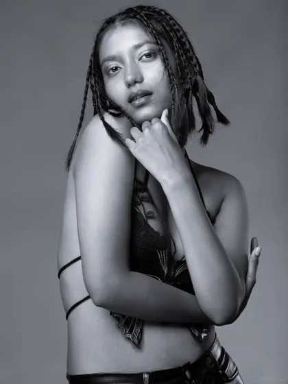 A black and white portrait of a model with braids and a butterfly top, with a soft and gentle pose.