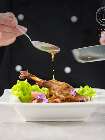 A chef artfully drizzles sauce over a perfectly cooked lamb shank. This image captures the essence of fine dining and the high level of culinary skill our team possesses.