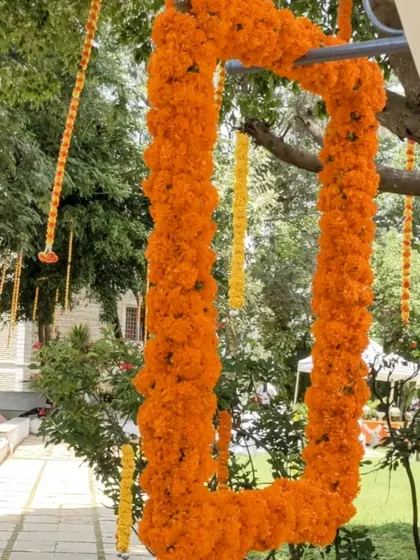 We create fun photo opportunities for your guests. This is a large, rectangular photo frame made entirely of bright orange marigolds, hung from a tree for a rustic and interactive decor element at an outdoor event.