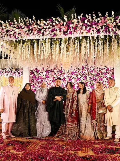 A perfect family portrait. The couple stands with their loved ones on the grand floral stage, a beautiful memory of togetherness from their special day.