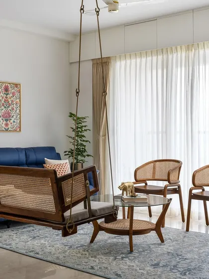 Another view of the 'Malhar' living room, highlighting the custom wooden swing with cane weaving, paired with matching chairs and a glass-topped coffee table.