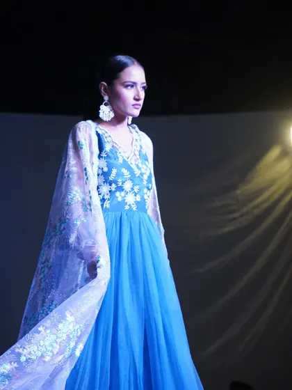 A model walks the ramp in a flowing blue gown with delicate floral embroidery on the cape.