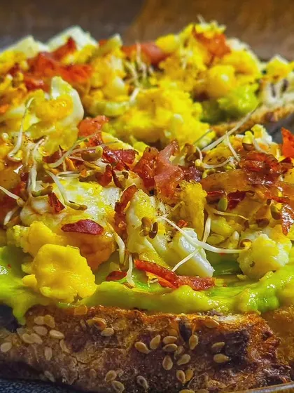 A close-up of the delicious layers on our avocado toast. You can see the creamy avocado, fluffy eggs, and crispy bacon.