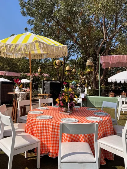 A Western-themed lunch setup with a red and white checkered tablecloth, a cheerful yellow and white striped umbrella, and simple white chairs.