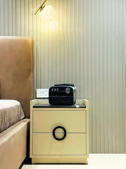 A close-up of a bedside table against a fluted wall panel. The simple, elegant design of the nightstand and the warm glow of the pendant light create a peaceful mood.