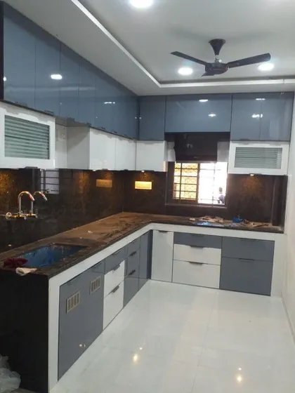 A U-shaped kitchen with a dual-tone design, using glossy grey and white cabinets. The perforated vegetable baskets are a practical addition for Indian homes.