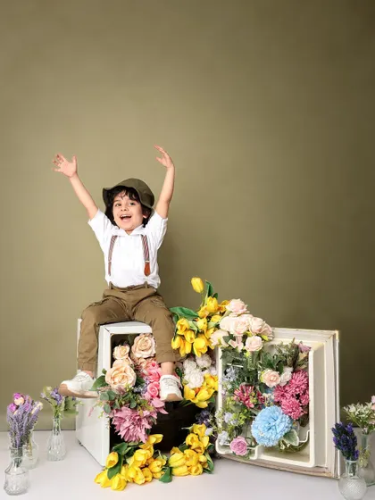 Hands up for fun! This energetic shot captures the boy's excitement as he sits atop the flower-filled fridge, creating a dynamic and happy memory.