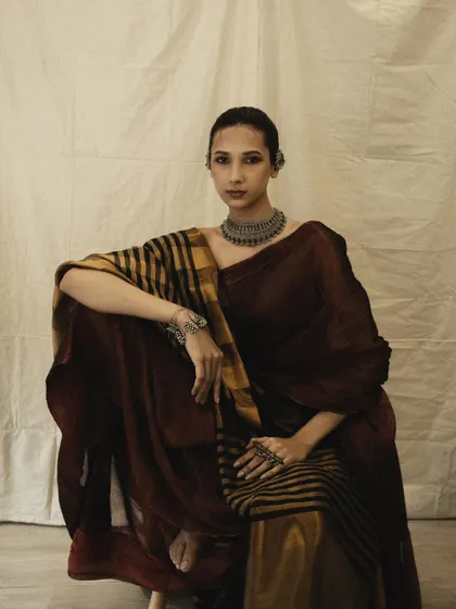 A full-look portrait with a muted, earthy color palette. The model's pose is graceful and strong, showcasing the complete ethnic ensemble.