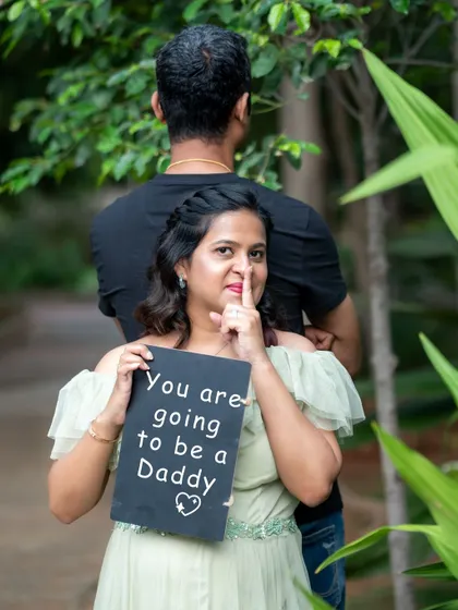 A playful and creative pregnancy announcement photo taken outdoors, with the mom-to-be holding a "You are going to be a Daddy" sign.