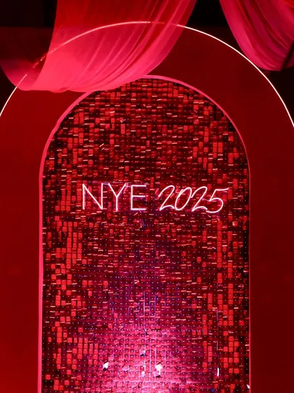 A chic photo booth with a shimmering red sequin backdrop and a 'NYE 2025' neon sign, perfect for capturing memories.