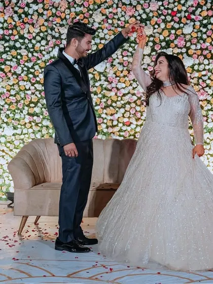 A couple shares a dance on their engagement night, in front of a beautiful wall of pastel flowers.