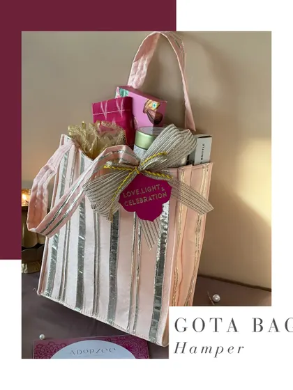 A stylish Gota Bag Hamper for Diwali. The pink and silver striped bag is packed with joy, sparkle, and a selection of handpicked sweets and goodies.