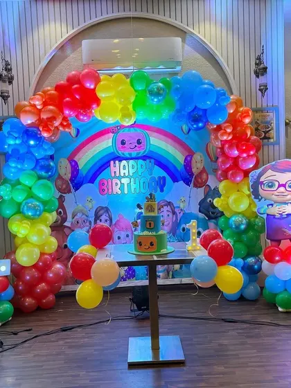 The complete Cocomelon party setup, including a themed cake table, character cutouts, and a large light-up number '1'.