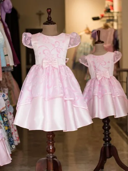 Another view of the matching pink dresses, highlighting the delicate floral pattern on the organza overlay and the sweet bow at the waist.