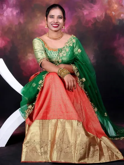 A vibrant solo portrait of a woman in beautiful traditional attire. The studio lighting makes the colors of the green and orange dress pop against the painted backdrop.