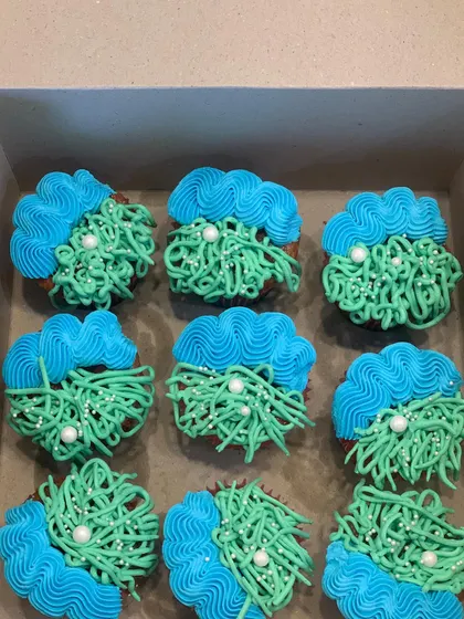 An abstract design for a modern celebration. These cupcakes feature a base of chocolate with green "grass" piping and a wave of blue buttercream, each dotted with a single white sugar pearl.