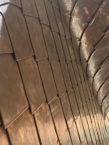 The undulating surface of the copper-tiled wall catches the light, highlighting the craftsmanship involved. This feature becomes a piece of art within the architecture itself.