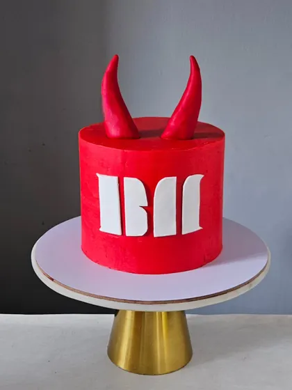 A bold and minimalist "Baby Monster" themed cake. The striking red fondant, clean lines, and simple devil horns create a modern and graphic look that really stands out.