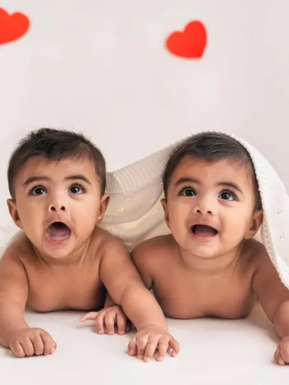 Peek-a-boo with two! These twin brothers are looking up with wide-eyed wonder from under a blanket, surrounded by hearts for their 6-month photoshoot.