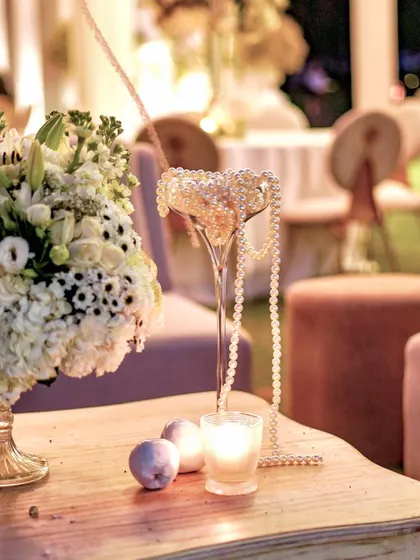 The same decor detail seen at night, with the soft glow of a candle adding a warm and romantic ambiance. The pearls and flowers catch the light beautifully.