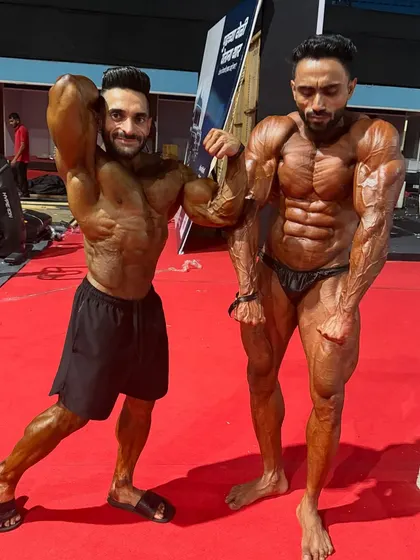 Hitting a front double biceps pose with a fellow competitor. This showcases arm size, chest fullness, and a sharp V-taper.