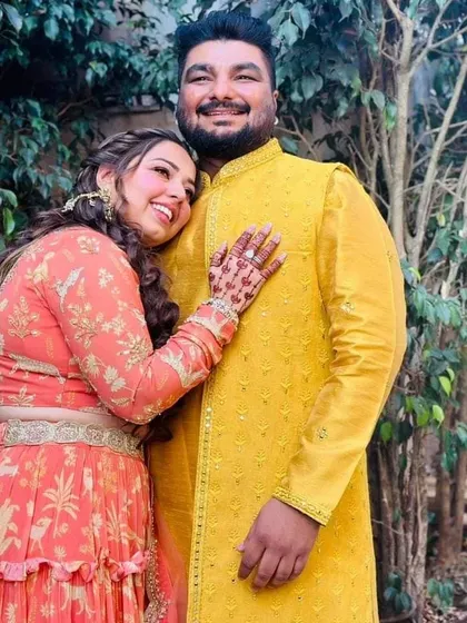 For their Haldi function, this groom wears a long yellow jacket with mirror work over a matching kurta, creating a bright and celebratory coordinated look with his bride.