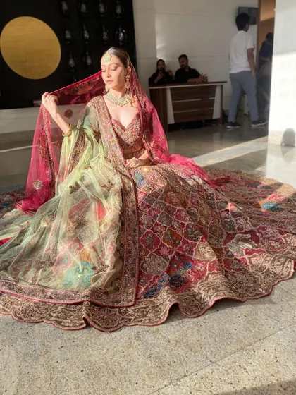 A wide shot capturing the magnificent trail of the bridal lehenga. The makeup remains a focal point, ensuring the bride's face is luminous and captivating even from a distance.