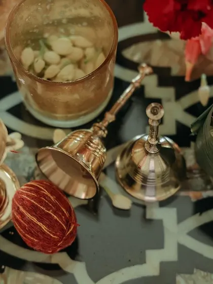 A collection of brass puja items, including a hand bell and small bowls, scattered among fresh flowers. These details are essential for creating a sacred atmosphere.