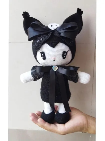 This is Kuromi from the Sanrio universe, made with black yarn and decorated with satin ribbons and a heart gem for a special touch.