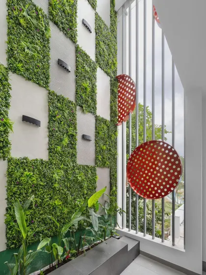 The triple-height courtyard acts as a balcony garden attached to the living room, extending the space outdoors. The vertical garden and perforated red metal discs create a visual delight accessible from every floor.