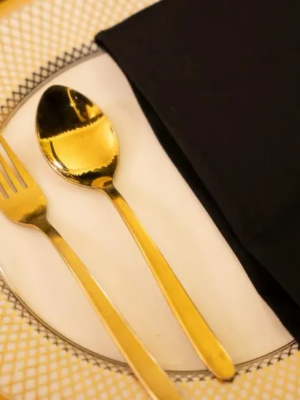 A close-up of our elegant place setting featuring gold-plated cutlery on a fine china plate with a gold rim. Every detail is chosen to reflect a standard of luxury and sophistication.