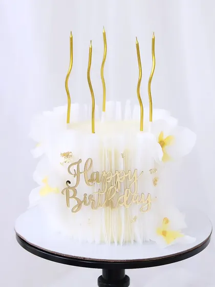 A pristine all-white birthday cake with a delicate, ruffled rice paper finish. The design is kept simple and elegant, topped with minimalist gold candles and a "Happy Birthday" sign.