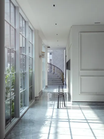 Sunlight streams through the large windows of this classical home, casting beautiful shadows across the polished marble floors. This corridor is a perfect example of how we use natural light to animate our spaces and create a sense of serene luxury.