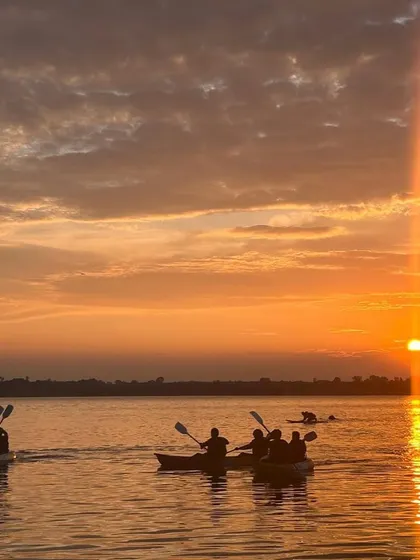 A group of kayakers paddles together as the sun sets, casting a warm orange glow over the water.