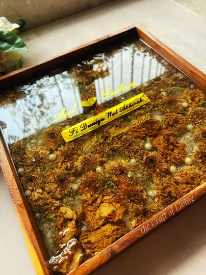 A top-down view of the marigold-filled wooden frame, showing the clear, glass-like finish of the resin. The pearls scattered throughout add a classic touch to the traditional flowers.