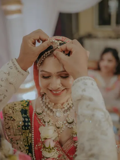 A close-up of a sacred wedding ritual. The groom gently places the maang tikka on the bride's forehead, a moment filled with tradition and love.