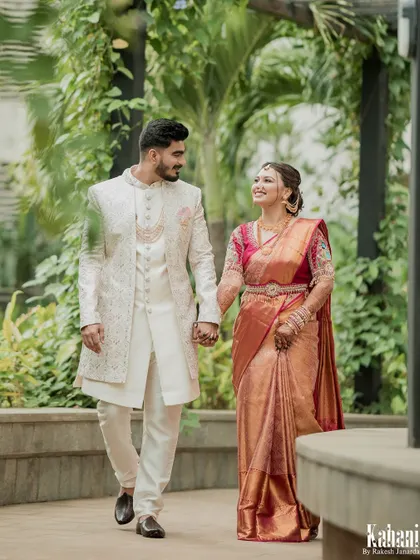 A perfect wedding portrait. The couple walks hand-in-hand, looking elegant and happy. The bride's complete look, from saree draping to hairstyle, is picture-perfect.