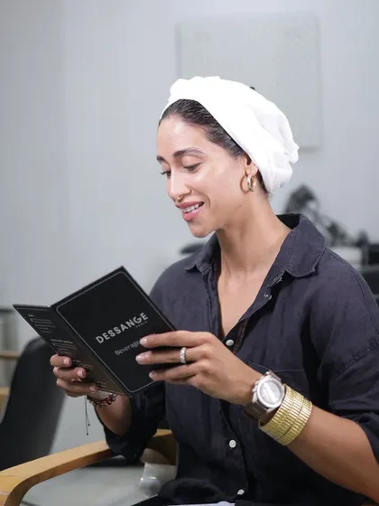 The little things matter. A client smiles while browsing our beverage menu, ready to enjoy a warm cappuccino or a refreshing iced tea during her hair spa. It's these small indulgences that complete the experience.