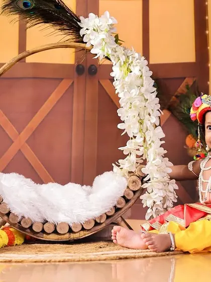 A beautiful pose of a baby boy in a colorful Krishna outfit, seated next to a floral-decorated hoop. I love combining traditional elements with artistic props to create unique images.