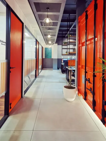 A corridor view showcasing the striking contrast between the bright orange container, glass-walled offices, and polished concrete floors. This composition of materials and colors defines the energetic and modern aesthetic of the workspace.