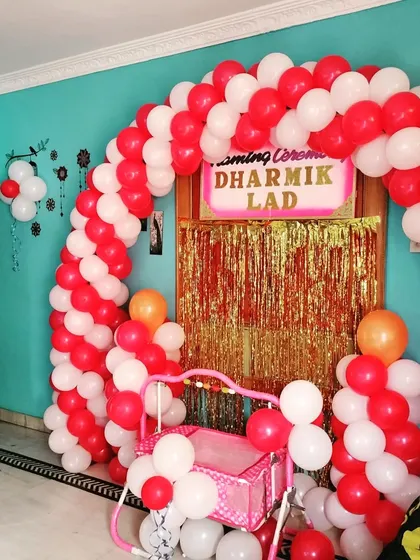 A bright and cheerful naming ceremony decoration for a home event. The red and white balloon arch frames the entrance, with a golden fringe curtain adding a bit of sparkle for the baby's cradle ceremony.