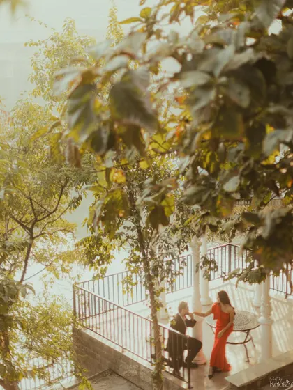 A romantic, fairytale-like scene of the groom kissing the bride's hand on a beautiful balcony surrounded by trees.
