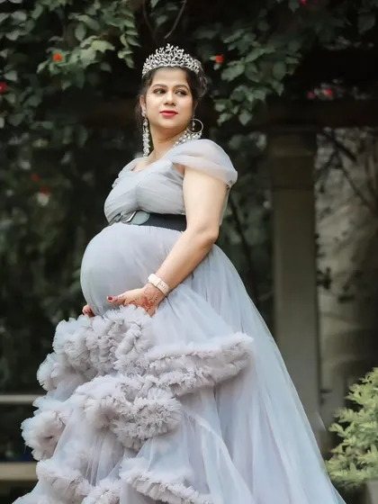 A serene and beautiful portrait of an expectant mother in a grey ruffled gown, surrounded by lush greenery.