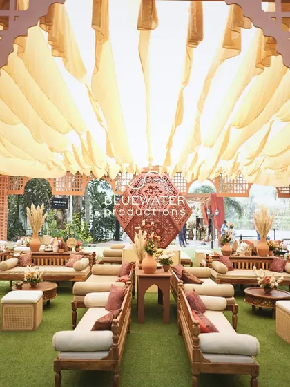 Looking through a rustic archway at the sprawling lounge setup, with a ceiling of soft, flowing yellow fabric creating a warm and inviting atmosphere.