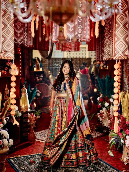 The bride shines in her colorful lehenga, standing in the immersive passageway of hanging rugs and lanterns.