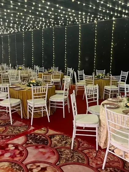 A wide view of a reception hall with a ceiling covered in fairy lights. The combination of the sparkling lights and classic white Chiavari chairs creates an elegant and enchanting space.