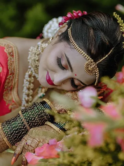 An artistic close-up of the bride, framed by flowers. This type of shot emphasizes the beauty of the bride's traditional look, including her gold jewellery, henna, and colorful saree, in a soft, romantic style.