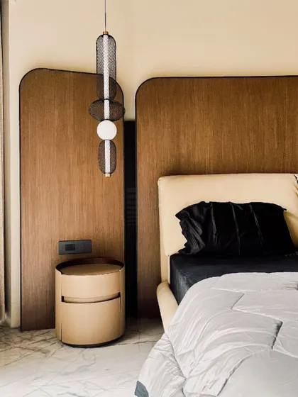 A harmonious blend of materiality and form defines this bedroom. A sculpted accent wall of rounded wood panels adds warmth and depth, complemented by a leather headboard and a sculptural pendant light for a sophisticated, timeless ambiance.