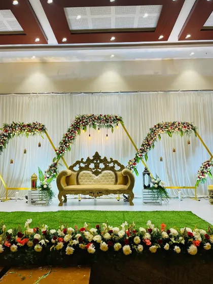 A wide view of a modern engagement stage with geometric floral arches. The green turf and ornate sofa complete this stylish and contemporary setup.